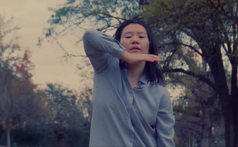 A woman is standing outdoors by trees in autumn
