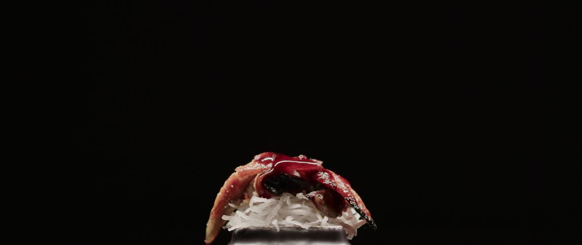 Red sauce drips over a slice of sushi against a black background