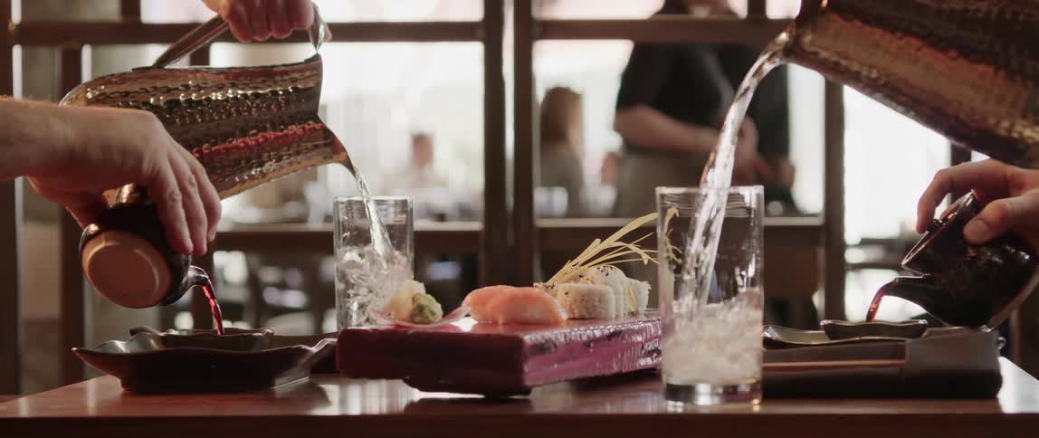 Servers place tray of sushi on table and fill water glasses