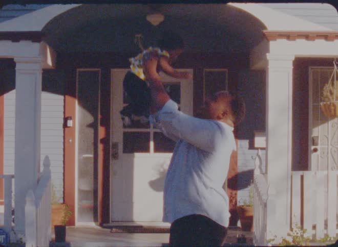 A father standing in front of his home tosses his baby daughter up in the air and catches her