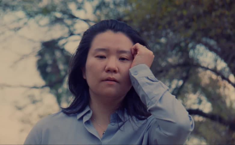 Woman standing outdoors moves her hand up her face in a dance like gesture