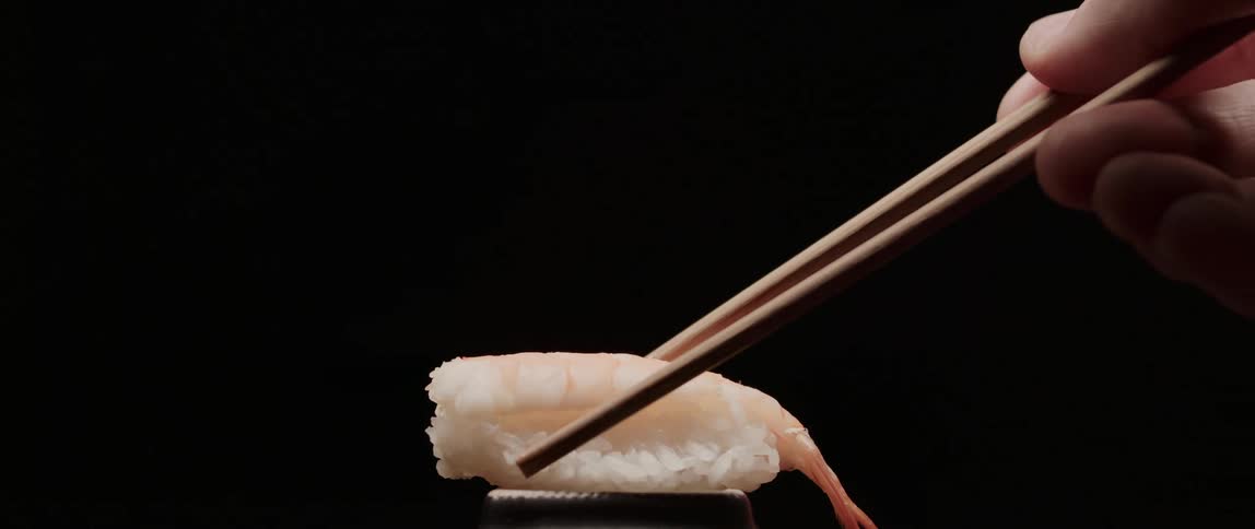 A woman sets a piece of sushi down with chopsticks and then picks it up again