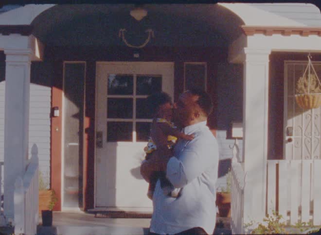 A man rocks his baby while standing outside of their house