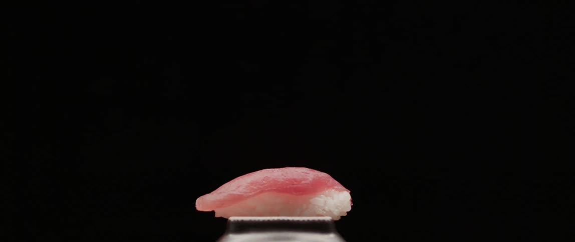 A piece of sushi plated in front of a solid background