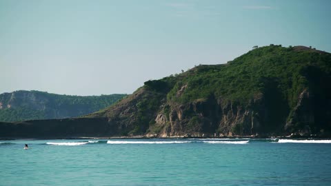 Waves roll in front of a green, rocky hill