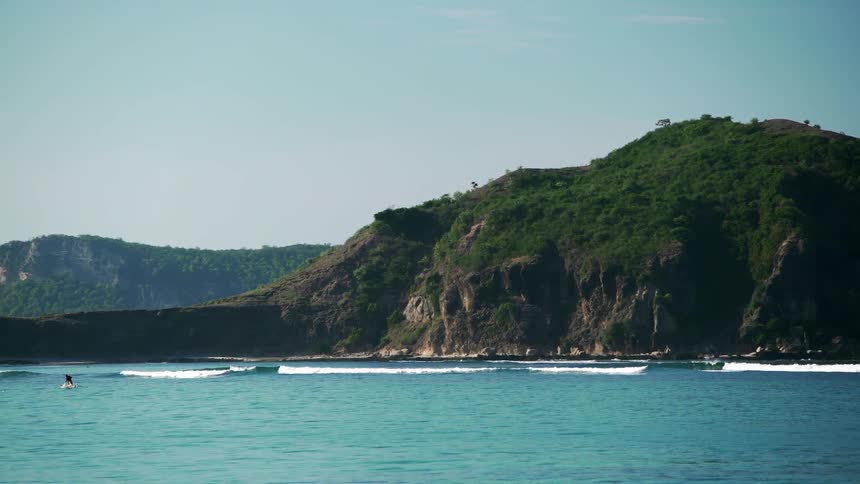 Waves roll in front of a green, rocky hill