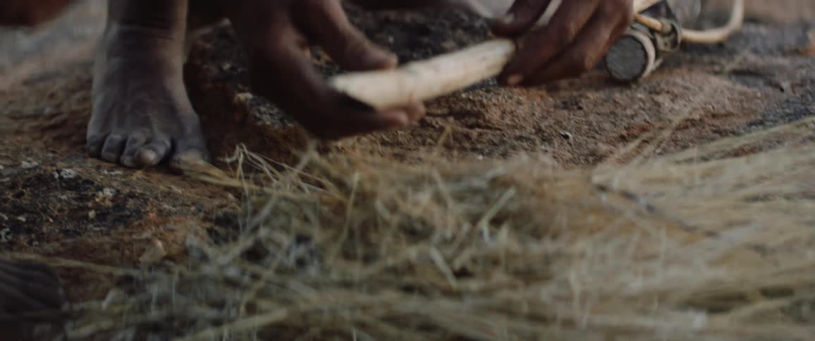 Bow hunters gather straw and place stick on it to prep a fire