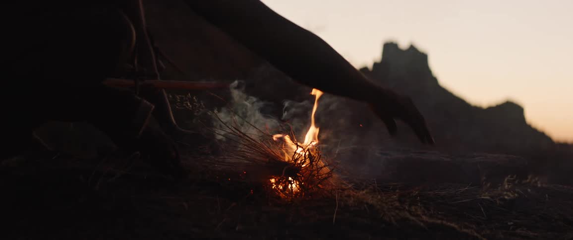 Young man stokes a fire with sticks and brush