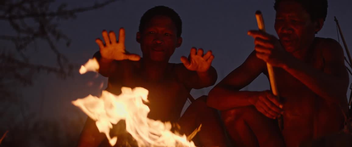 Two tribal men sit around a fire in the evening