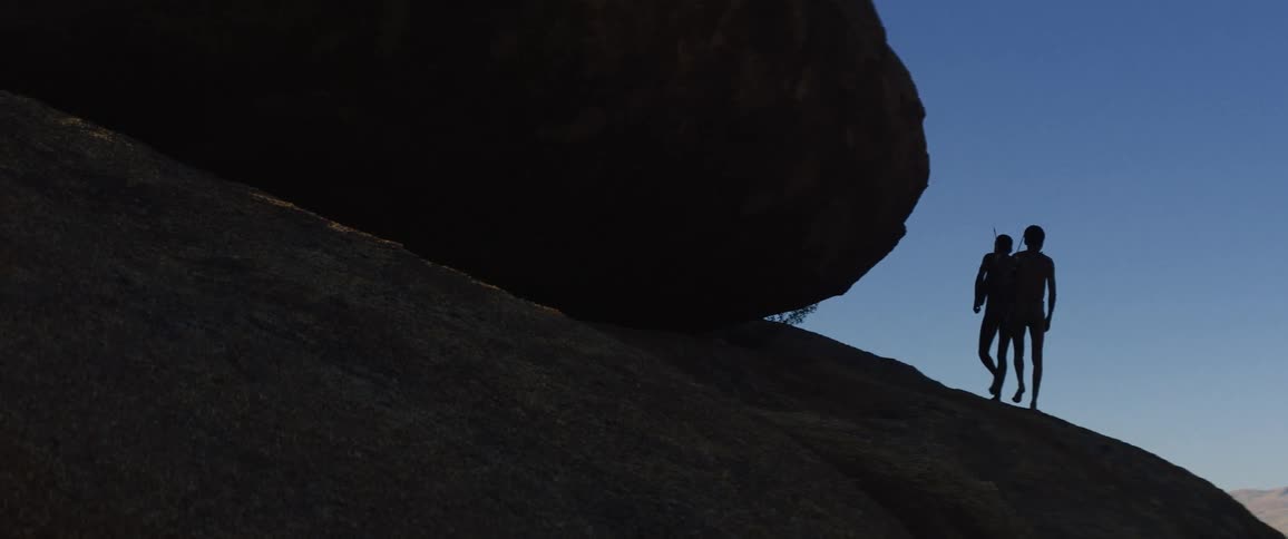 Tribal men walk on hill slope next to big rock