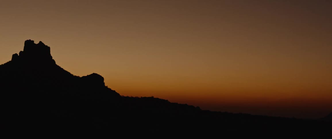 Mountain silhouette stands against red horizon at night