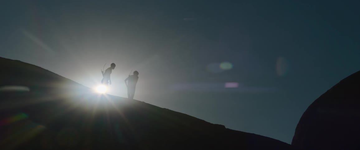 Sun shines over slope turning two men into silhouettes