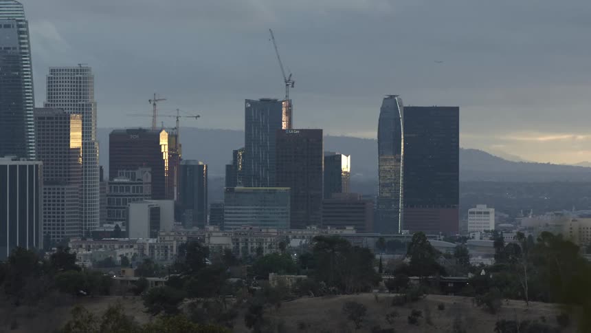 Construction cranes work on skyscrapers in downtown backed by misty mountains