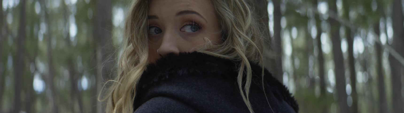 A woman in the woods whips her aroundlooking over her shoulder with frightened eyes