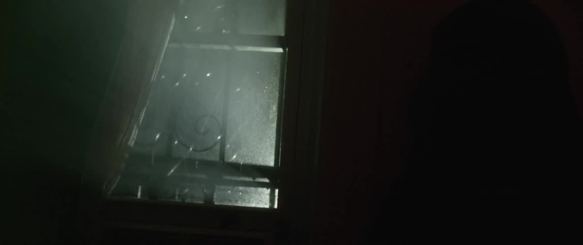 A man picks out two windows in a home with police lights flashing outside