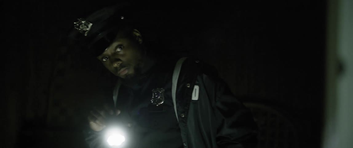 An officer is searching a dark home with a flashlight