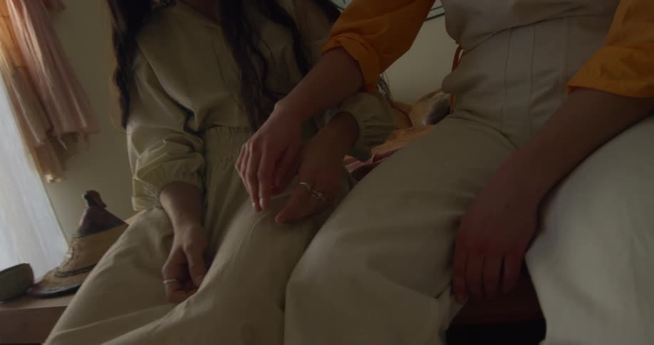 Two girls sitting side by side play with each others hand and fingers