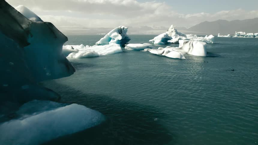 Icebergs and broken ice are floating in arctic waters and there are mountains in the distance