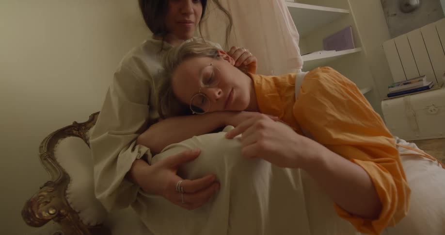 Blonde woman sits on floor with her head in sitting womans lap
