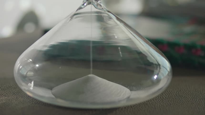 Sand flows through hour glass sitting on textured surface