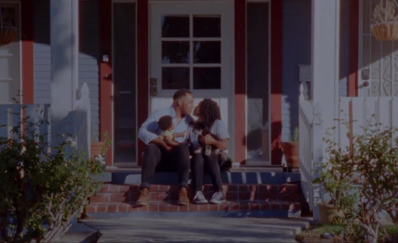 Parents kiss as they sit on front porch steps holding child and dog