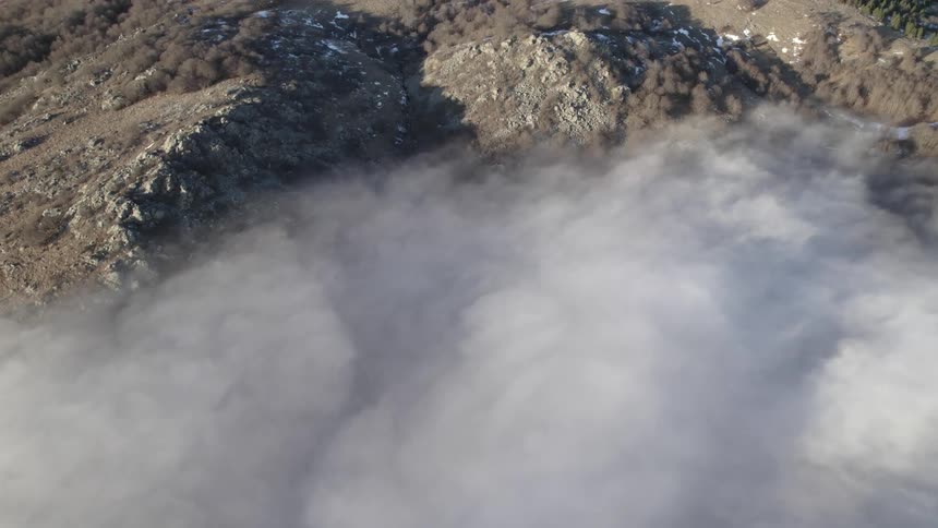 A thick layer of cloud cover clears to reveal snow dotted ridges and peaks