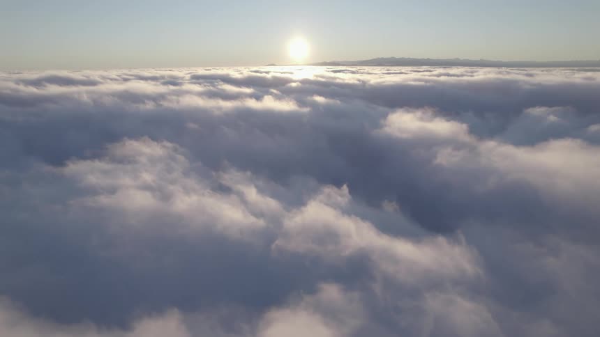 Aerial view of the sun above the clouds and mountains in the distance