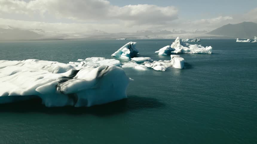Icebergs and broken ice are floating in arctic waters and there are mountains in the distance