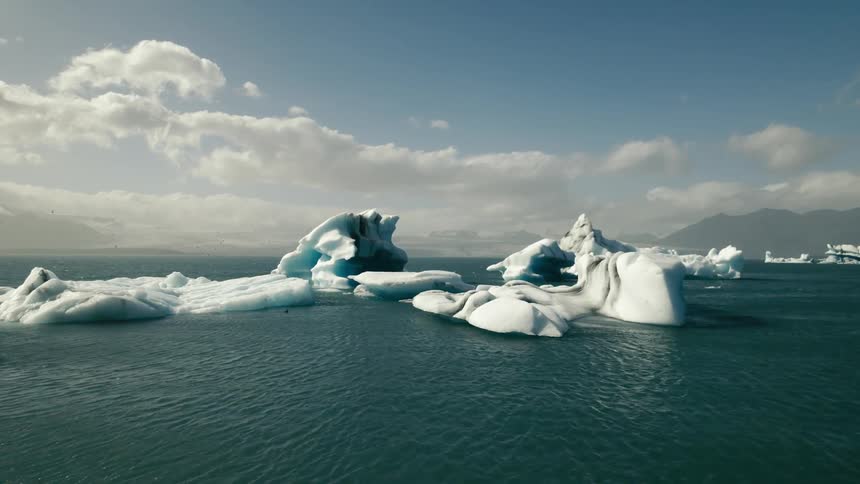 Icebergs and broken ice are floating in arctic waters and there are mountains on the horizon