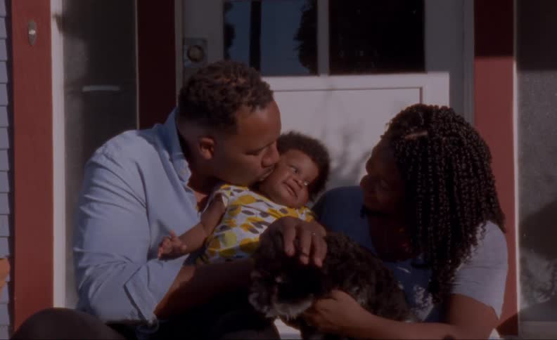 A young family with a baby petting their dog on a front porch