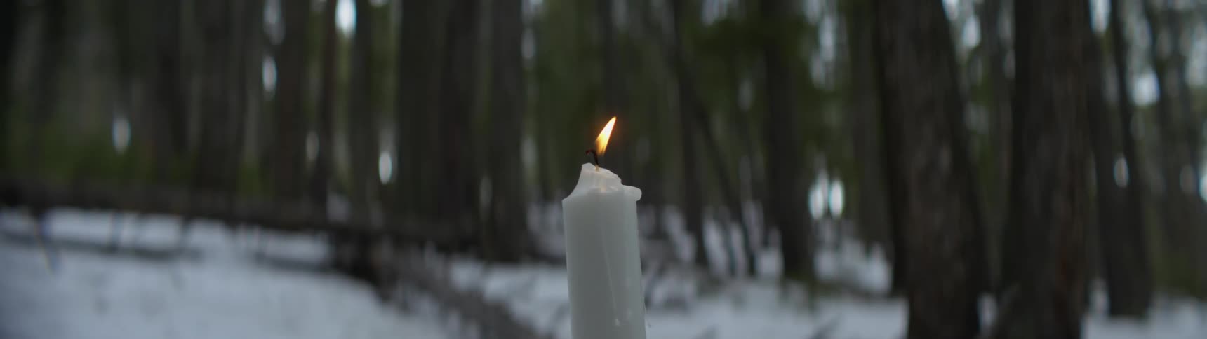 Candle burning in the middle of the snow covered forest blows out