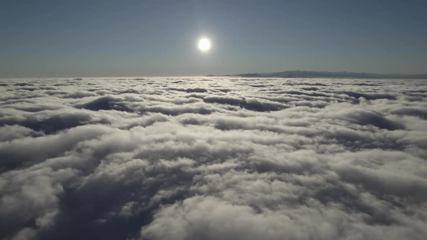 Aerial view of the sun above the clouds and mountains in the distance