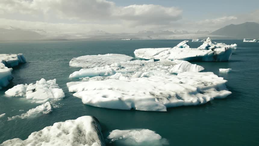 Icebergs and broken ice are floating in arctic waters and there are mountains on the horizon