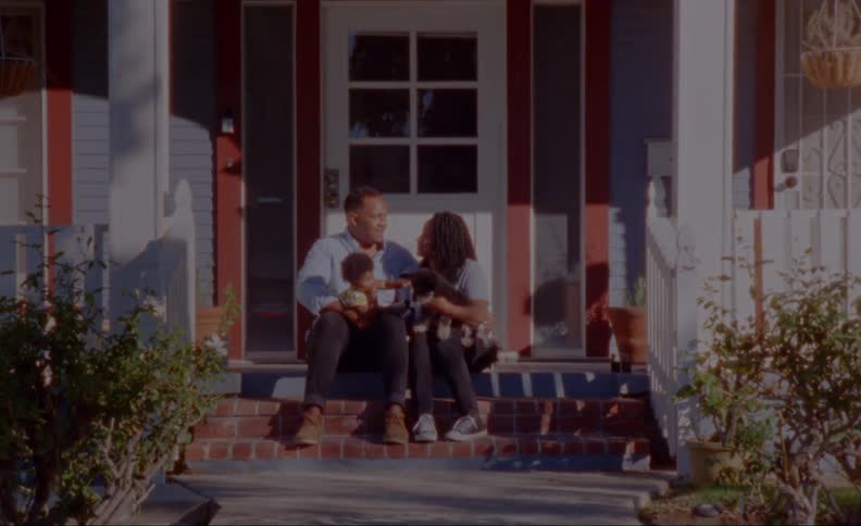 Parents talk as they sit on porch steps with toddler and pet dog