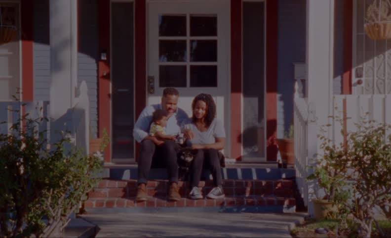 A family of three is sitting outside of their home