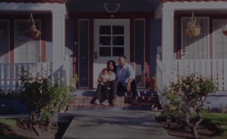 Parents exchange looks as they sit on front porch with child and pet dog