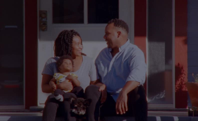 Parents sit on porch with dog and child as they look into each others eyes