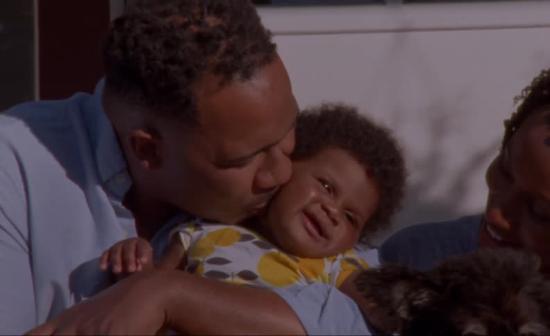 A man kisses his baby daughter on the cheek as he sits outside with his wife and dog