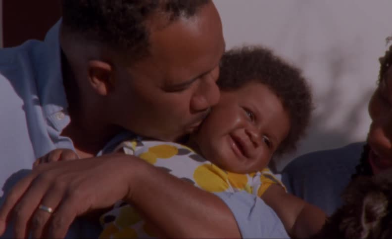 A man sits next to his wife and kisses their baby daughter