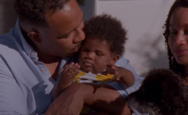 Dad kisses the baby as mom smiles while petting the dog
