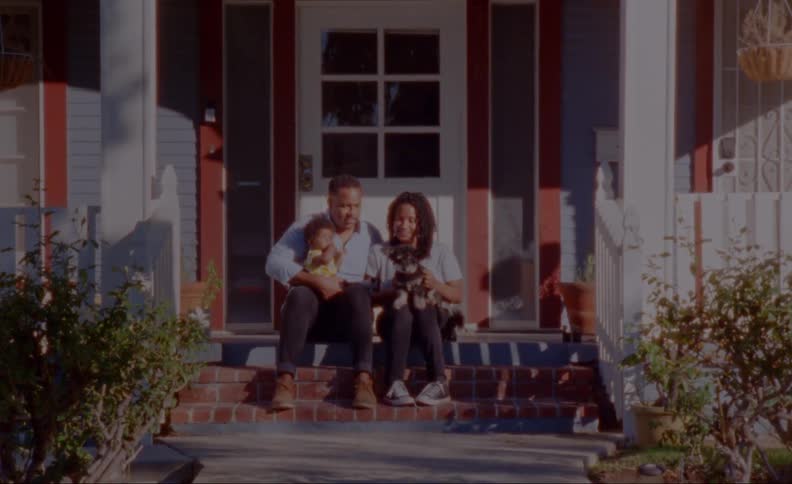 Family sits on front porch steps holding their child and their pet dog