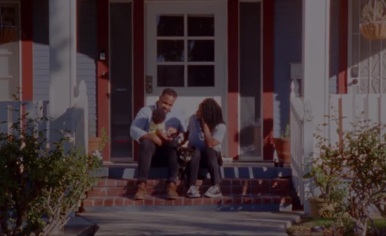 A family sitting on the front steps of their home with dad holding baby and puppy in between