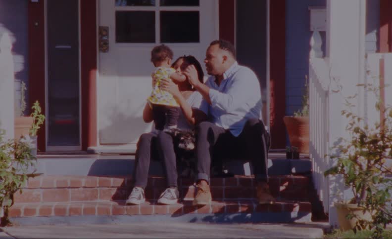 Mother and father play with toddler as they sit on porch with their dog