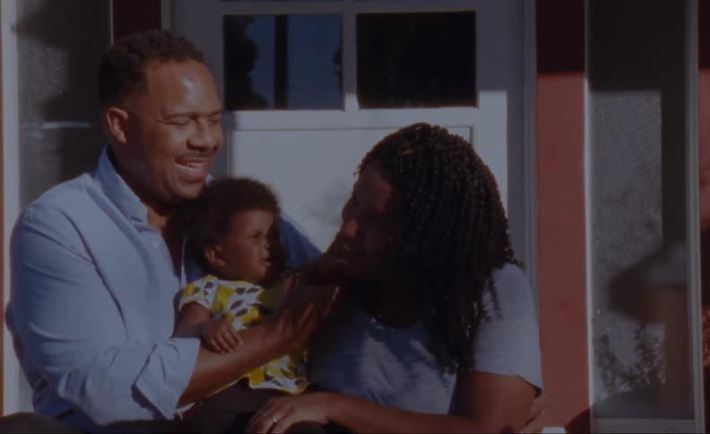 Parents laugh as their baby son grabs their faces as they pose on their front porch