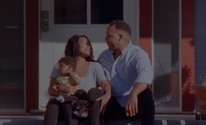Family sits on front porch steps with dog as parents turn to look into each others faces