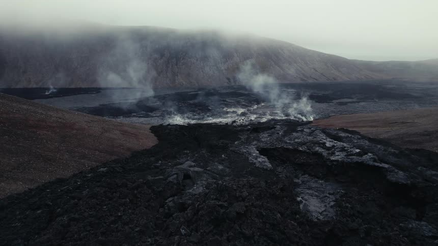 Smoke rises from ash remains of lava flow on foggy day