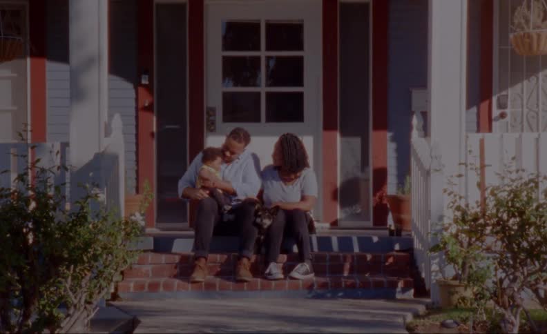 A man holds his baby while sitting with his wife on their front porch