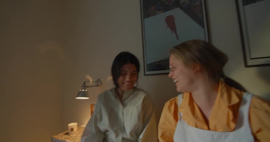 Two girlfriends sitting on a bed talking and laughing together