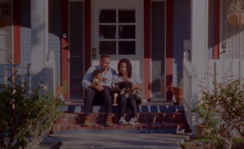 A young family with a baby posing with a dog on their front steps