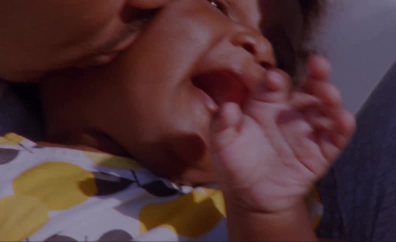 A baby tries to move away as his father kisses his cheek